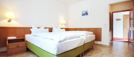 Habitación de hotel con una cama verde, cabecero de madera, dos mesitas de noche y dos lámparas de pared.