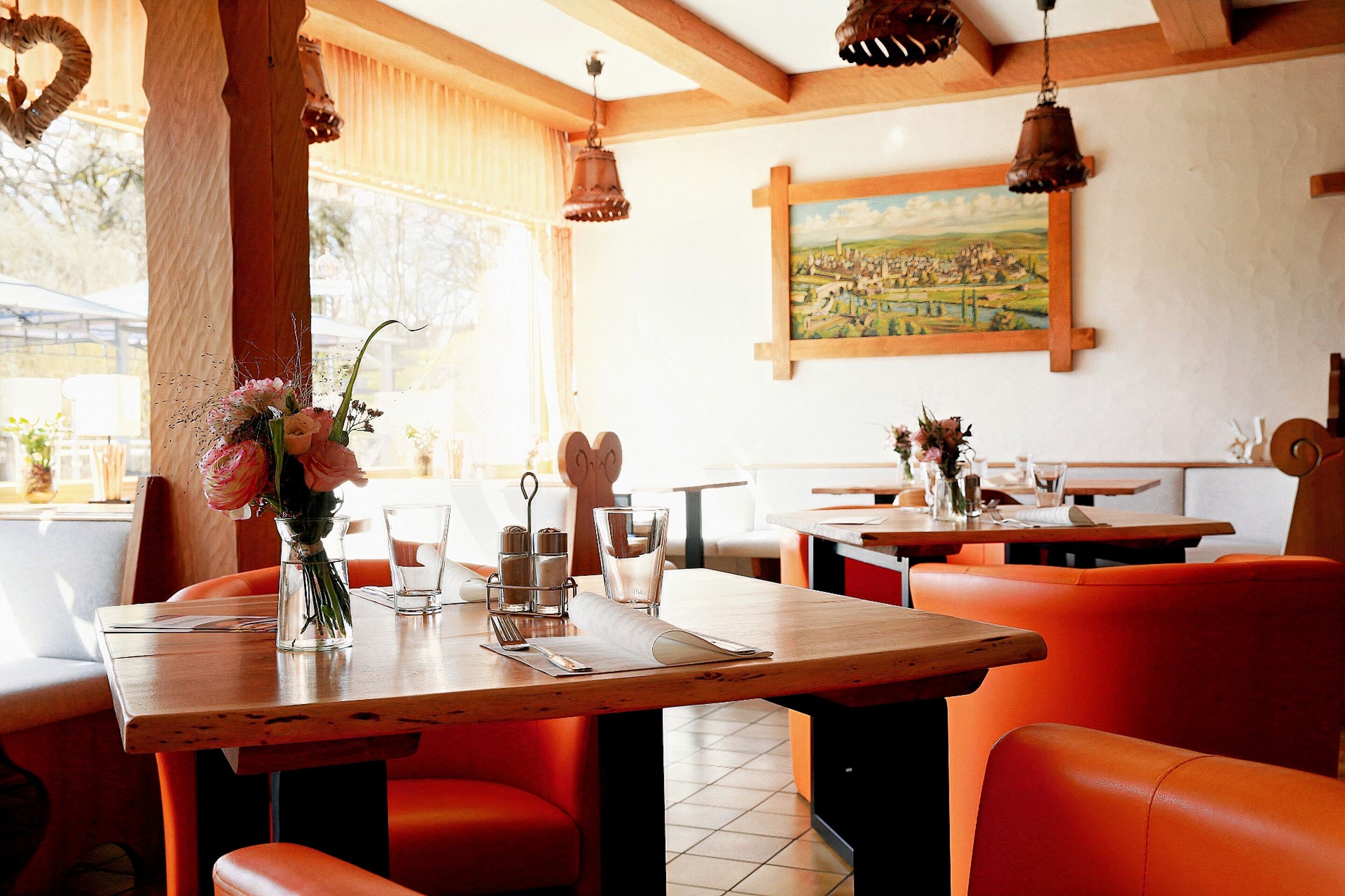 Interior de un restaurante con mesas de madera, asientos tapizados en color naranja y un cuadro en la pared.