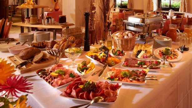 En frukostbuffé med ett varierat utbud av mat, inklusive kött, ostar, frukt och bakverk.