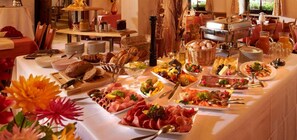 Un bufé de desayuno con diversos alimentos, como carnes, quesos, frutas y bollería.