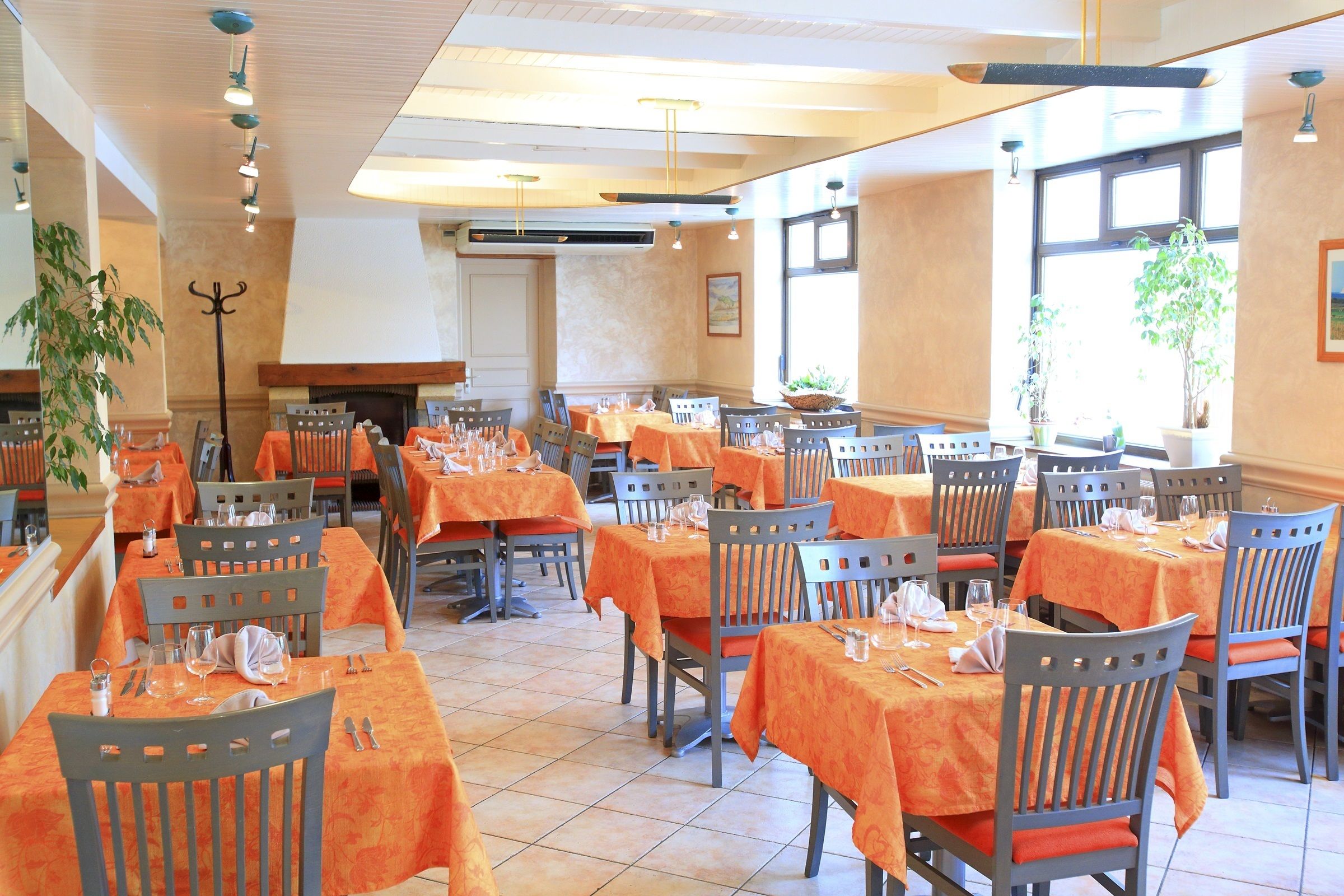Un restaurant avec de nombreuses tables recouvertes de nappes orange, disposées en rangées et accompagnées de chaises.