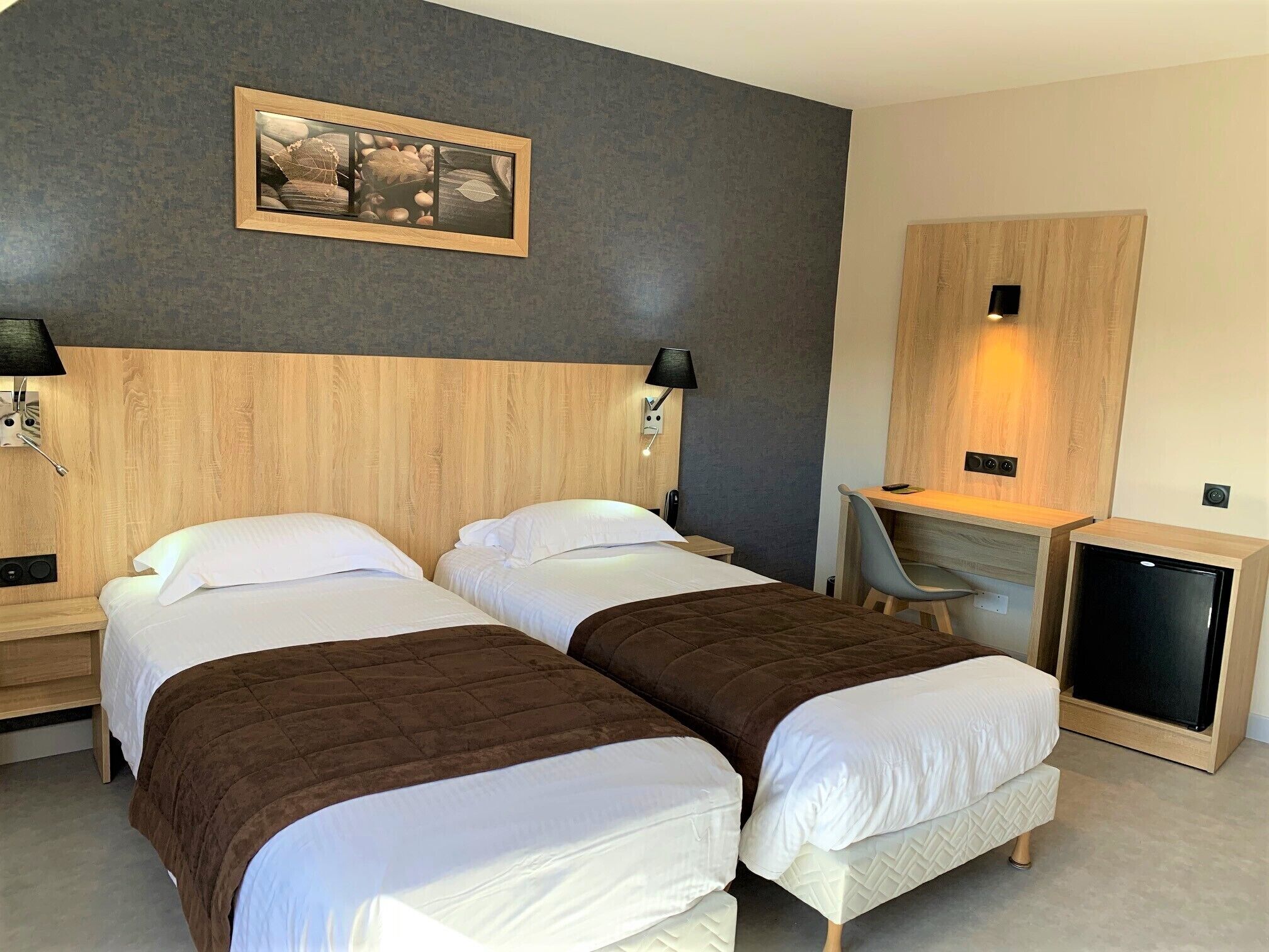 Ein Hotelzimmer mit zwei Betten, einem Schreibtisch, einem Stuhl, einem Fernseher und einem gerahmten Bild an der Wand.