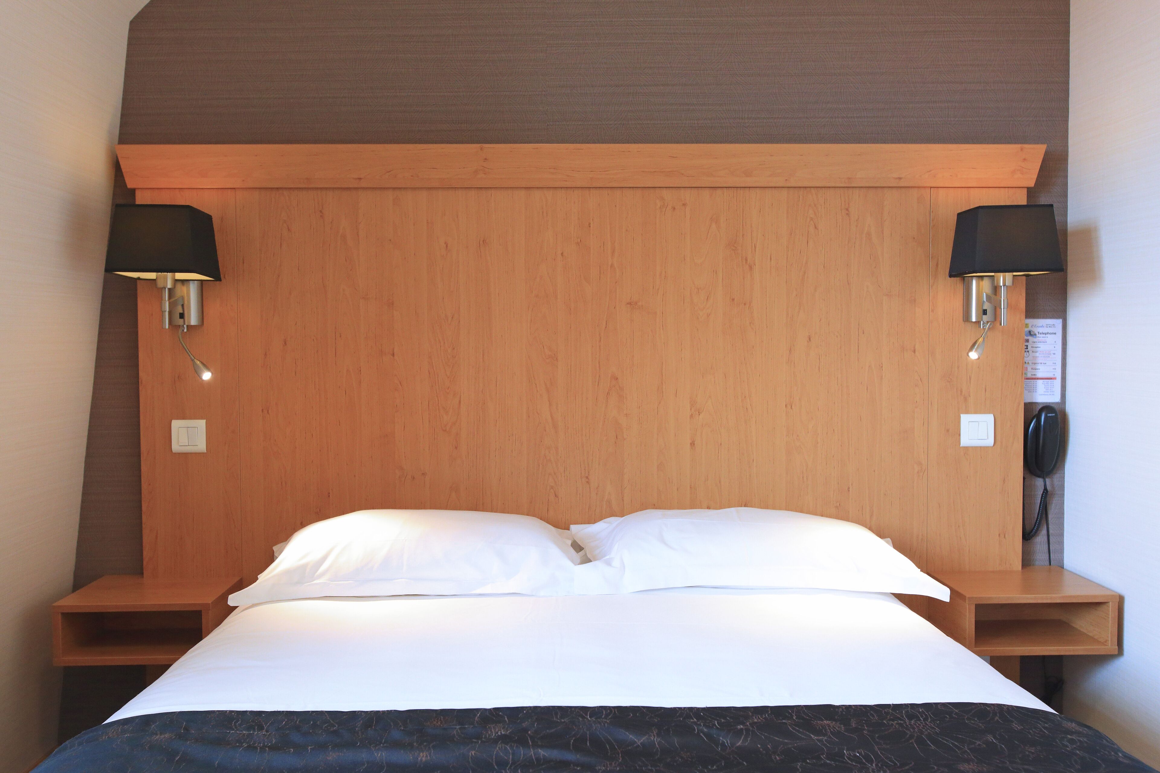 Una cama bien hecha con sábanas blancas, dos mesitas de noche con lámparas y un cabecero de madera.