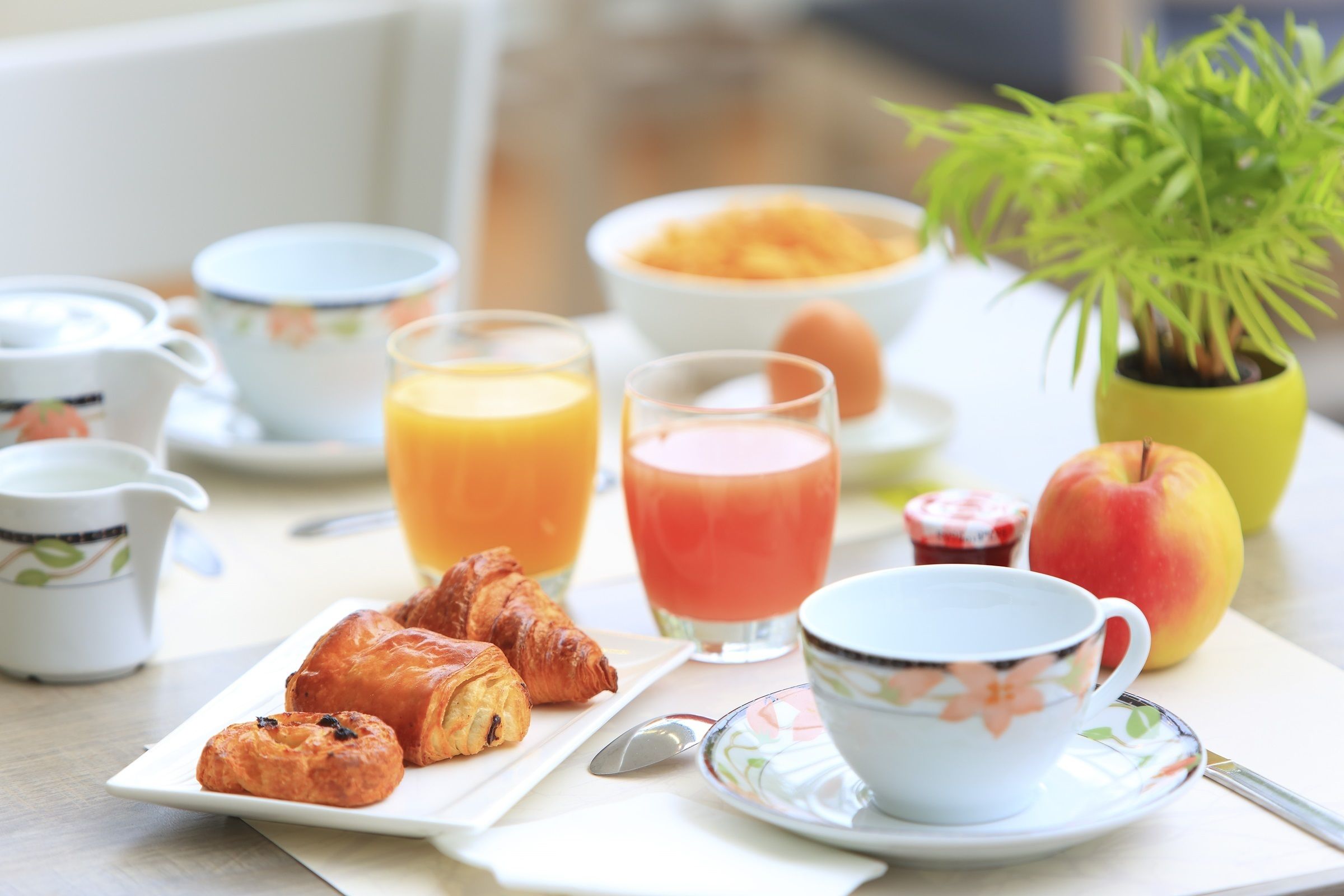 A breakfast table with croissants, a cup, a bowl of fruit, and a glass of orange juice.