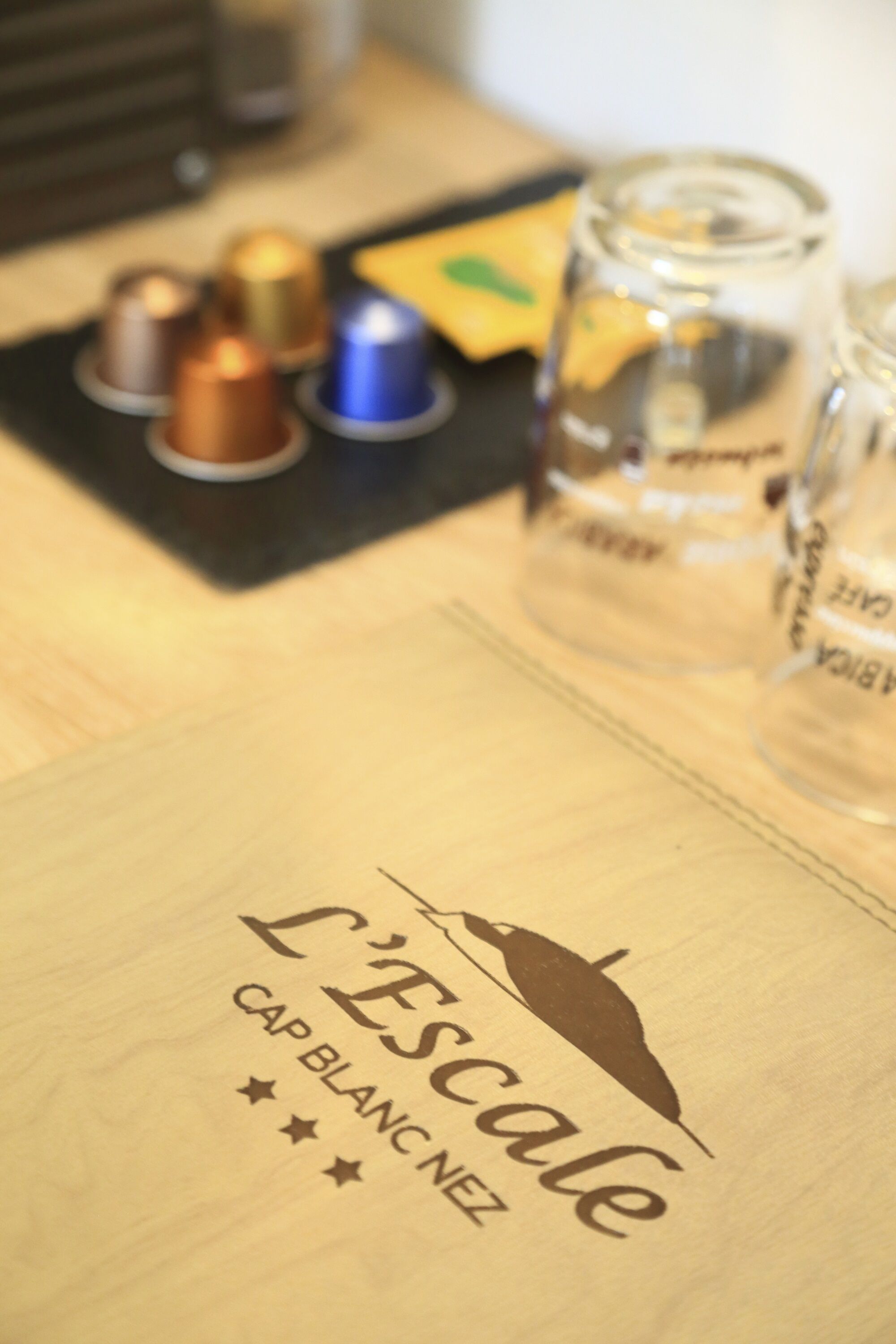 A wooden table with a logo reading "L'Escalade Cap Blanc Nez" and a few items including a glass jar and some metallic objects.