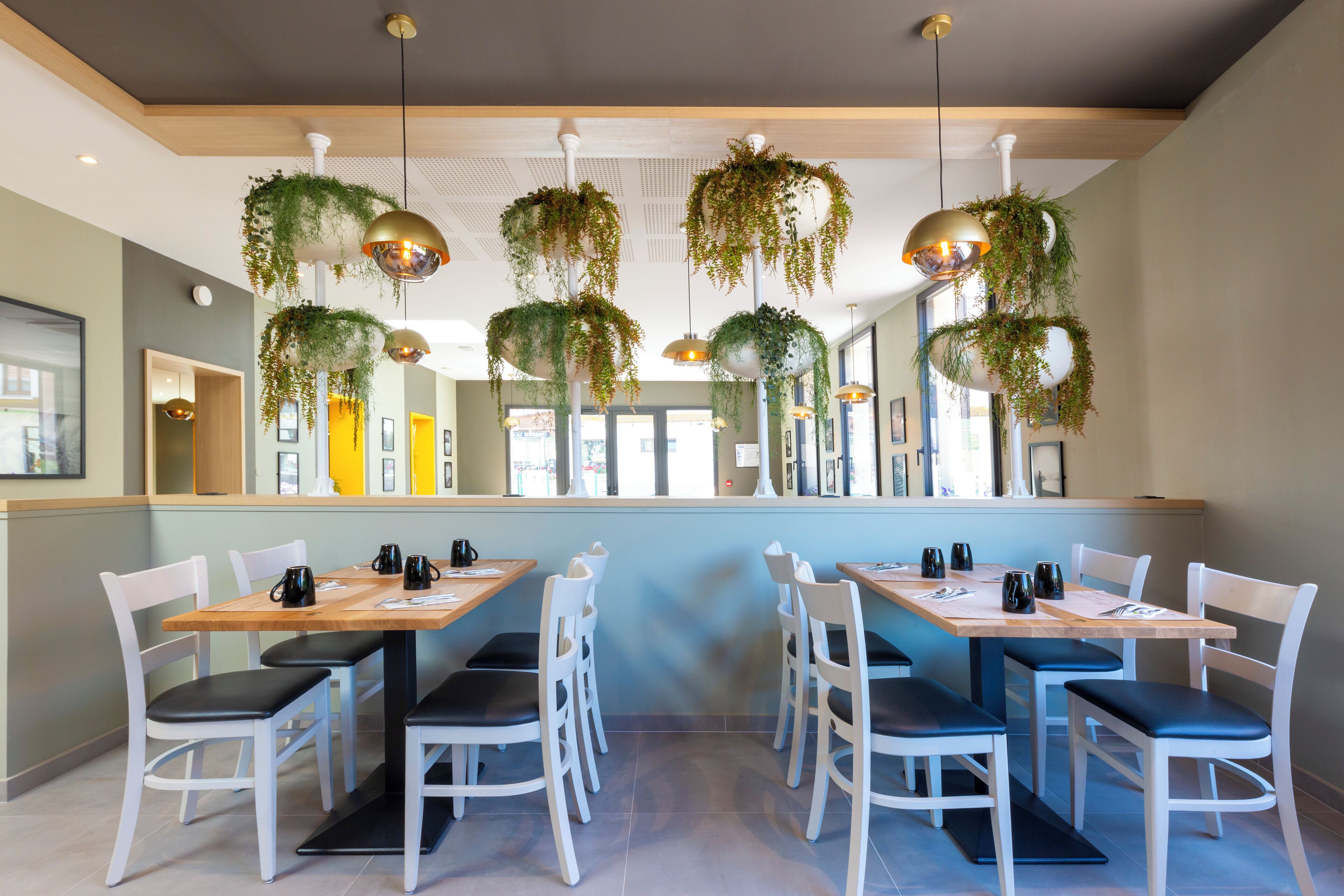 Un restaurant avec des chaises blanches, des tables en bois, des plantes suspendues et des luminaires suspendus.