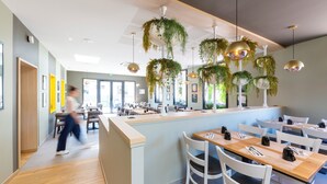A modern restaurant interior with a central counter, white chairs, hanging plants, and pendant lighting. - Hôtel L'Escale (Escalles)