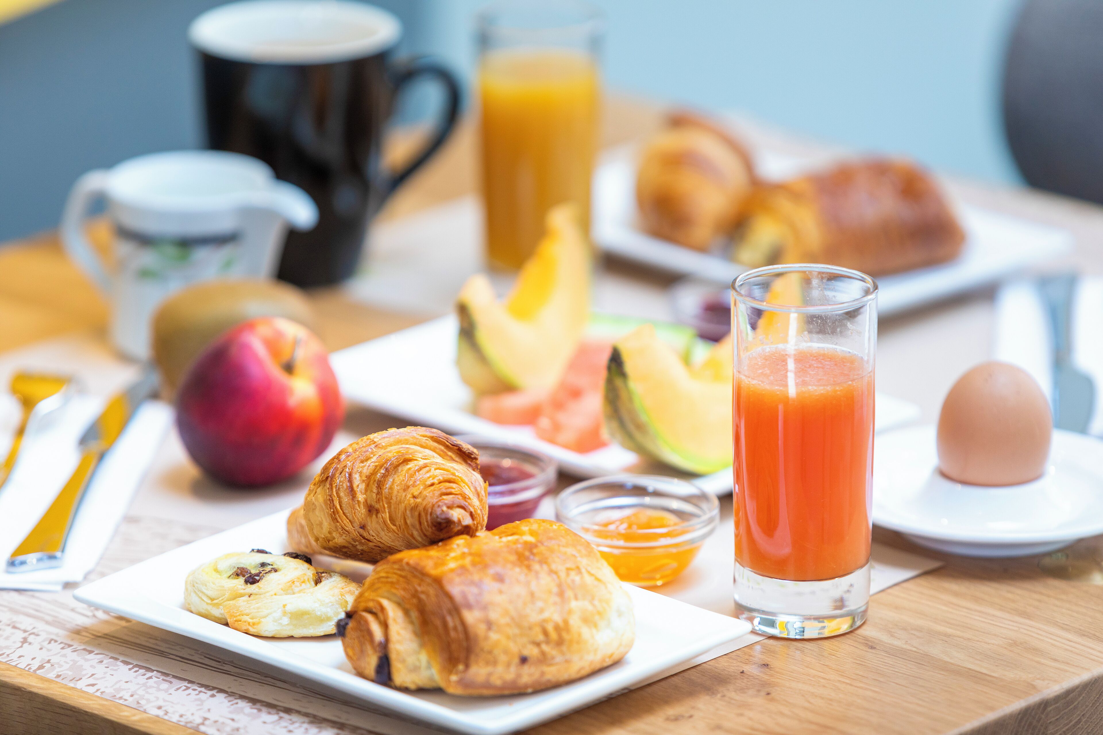 Una mesa de desayuno con croissants, fruta, un vaso de zumo de naranja y una taza de café.