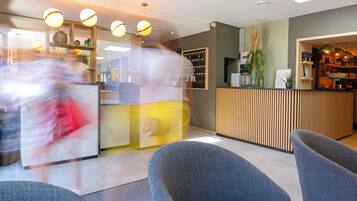Een moderne receptie met een houten receptiebalie, een zithoek met blauwe stoelen en hanglampen.