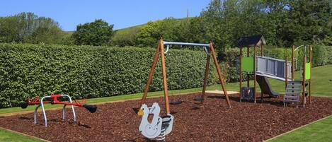 Une aire de jeux avec des balançoires, un toboggan et une structure d’escalade.