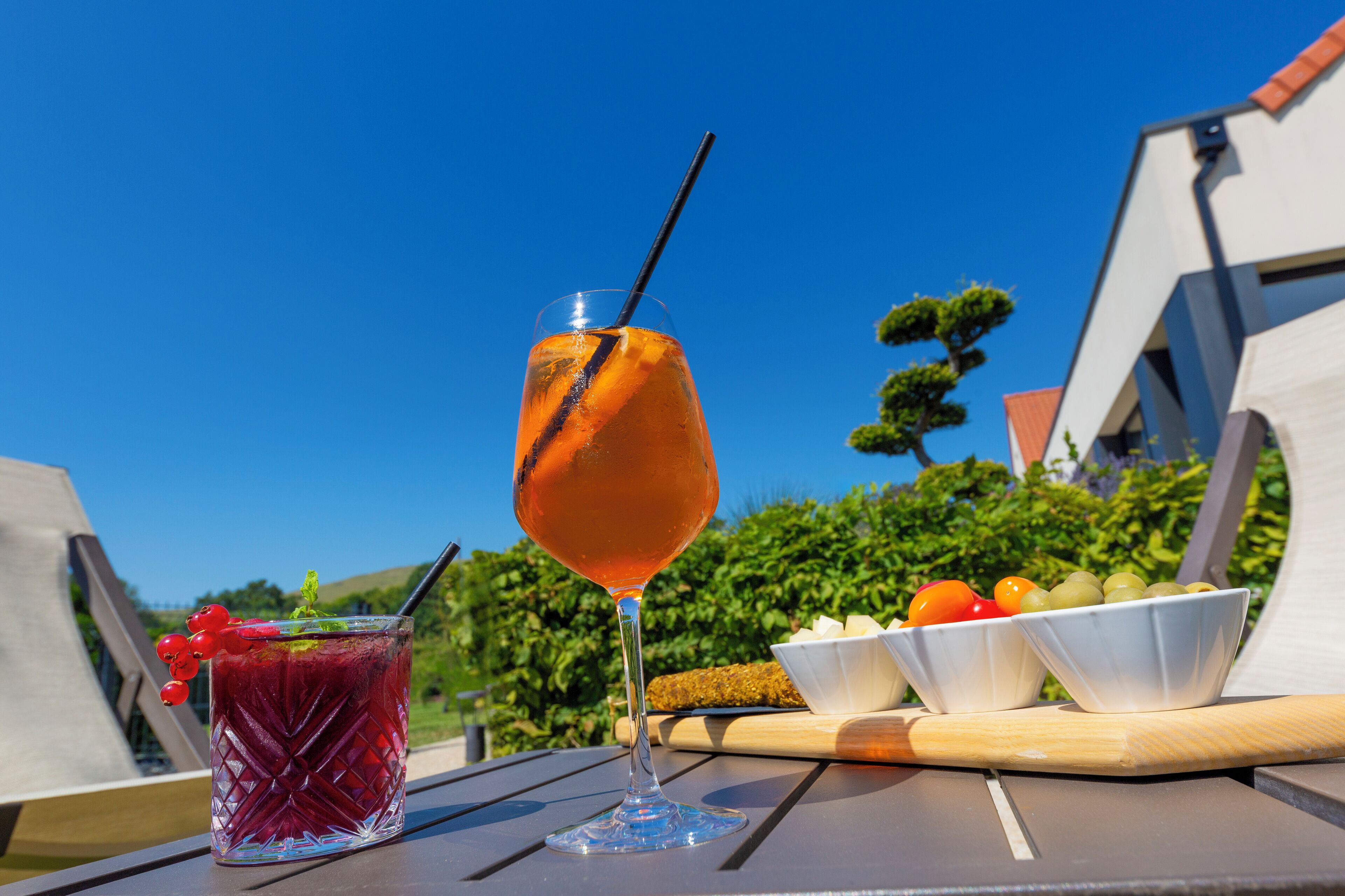 Um copo de bebida de laranja com canudo sobre uma mesa com uma tigela de frutas e uma tábua de madeira.