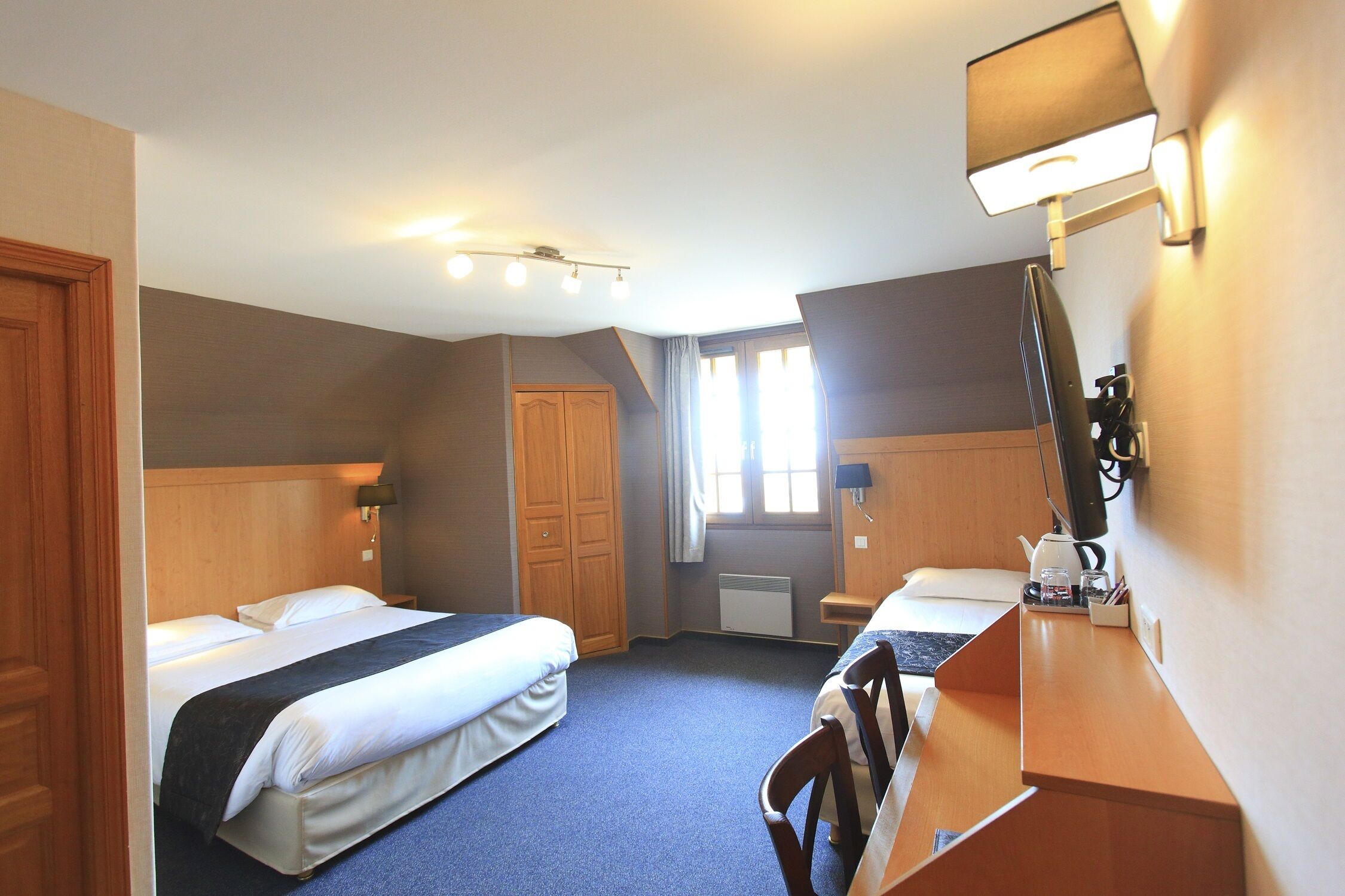Habitación de hotel con dos camas, un escritorio, una silla, una lámpara de escritorio, un espejo y una ventana con cortinas.