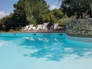 A swimming pool with clear blue water, surrounded by white lounge chairs and a stone wall. - Tenuta di Spannocchia (Chiusdino)