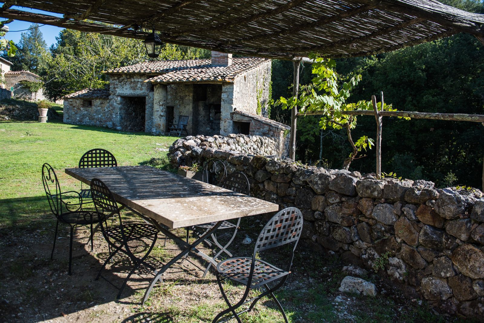 An outdoor dining area with a stone wall, a table, and metal chairs.