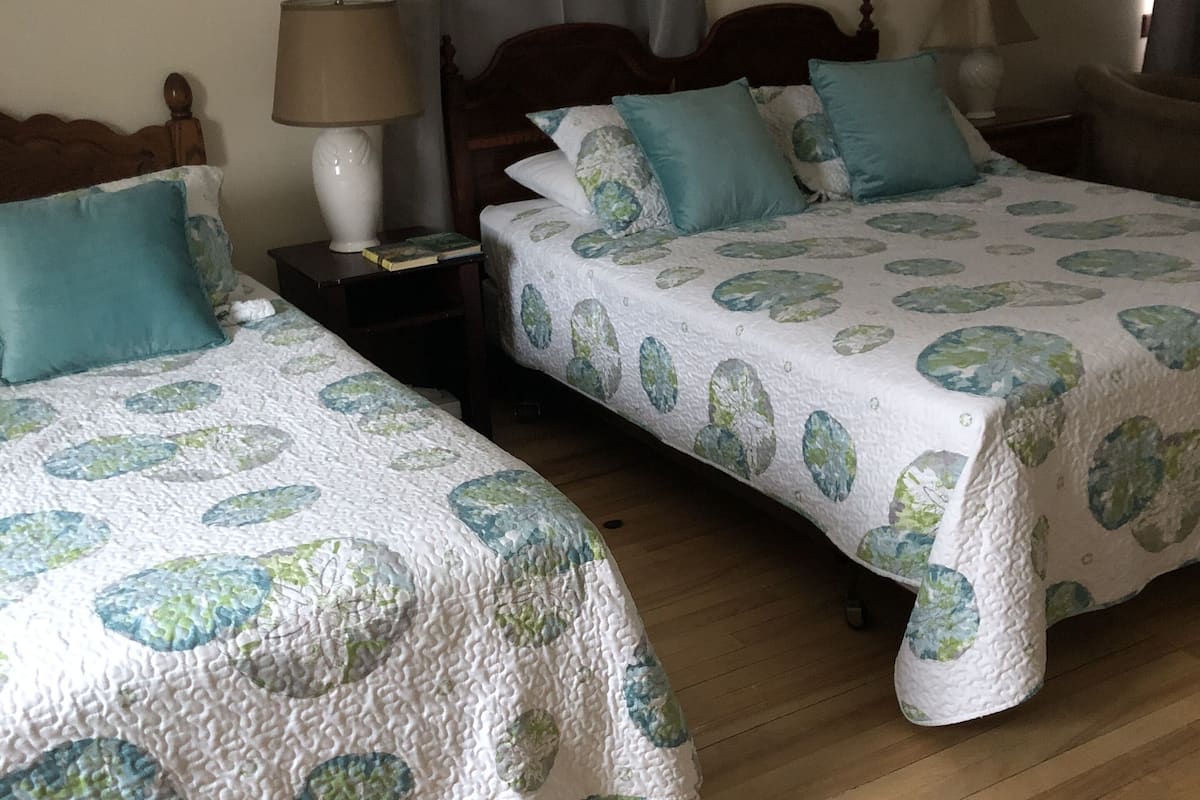Two beds with matching floral bedding, wooden headboards, bedside tables with lamps, and a wooden floor.