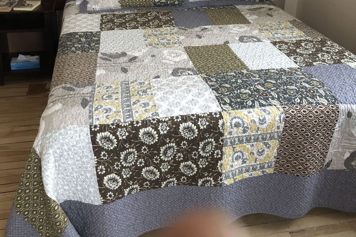 A bed with a patchwork quilt, a wooden headboard, and a nightstand with a lamp and a book.
