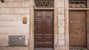 A brown door with a metal grille and a brass knocker, set in a stone building with a number '36' above it. - Residenza Costaguti (Rome)