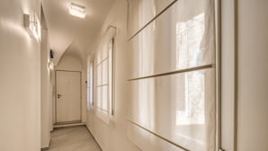 A hallway with a door at the end, large windows, and a light fixture on the wall. - Residenza Costaguti (Rome)