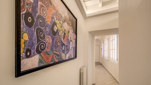 A hallway with a large abstract painting on the wall, a radiator, and a view of another room through an arched doorway. - Residenza Costaguti (Rome)