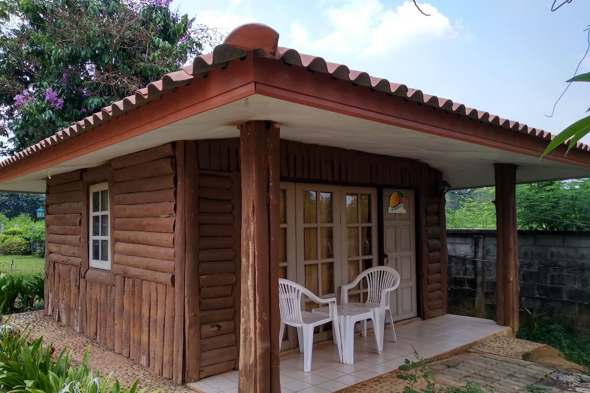 A wooden cabin with a tiled porch and two white plastic chairs.