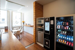 A modern kitchen with a wooden counter, white chairs, a microwave, and a beverage vending machine. - Turista da Trindade (Porto)