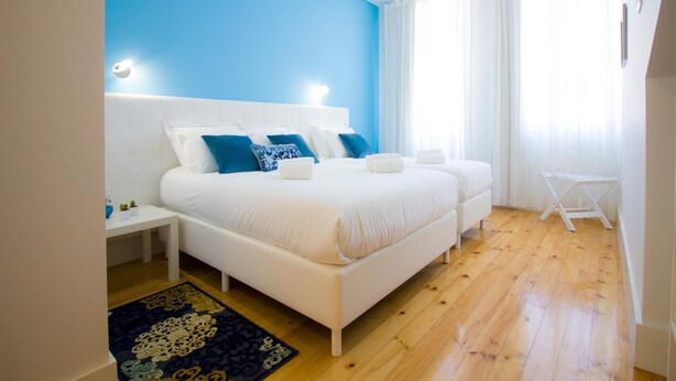 A bedroom with a large bed, a bedside table, a small table, and a window with curtains.