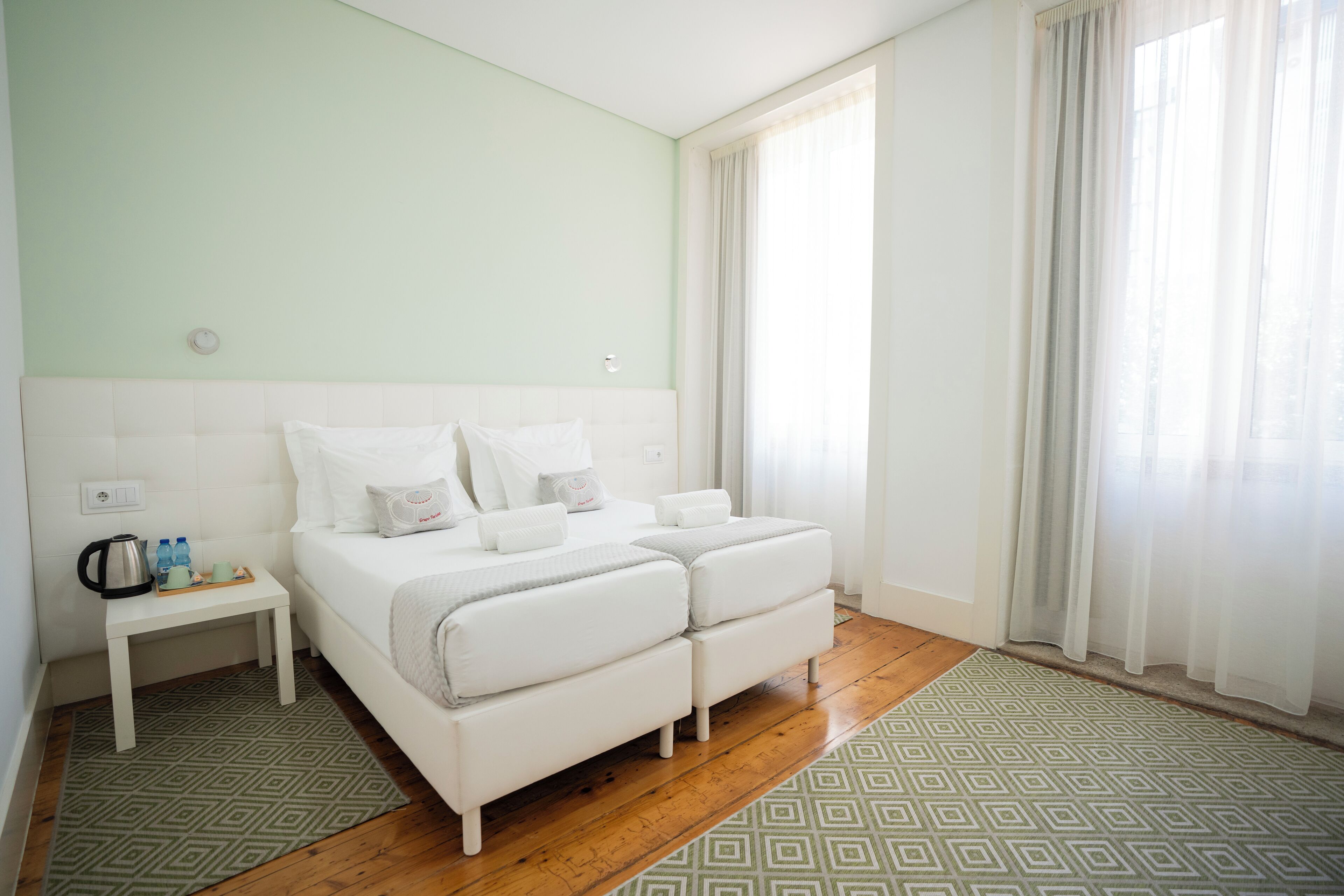Quarto com cama, mesa de cabeceira e janela com cortinas.