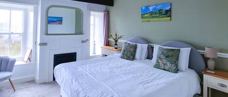 A bedroom with a large bed, a bedside table, a chair, a fireplace, and a window.