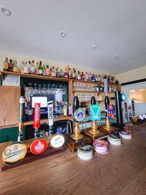 A bar with multiple taps, shelves of liquor bottles, and glasses. - Red Lion Inn (Wooler)