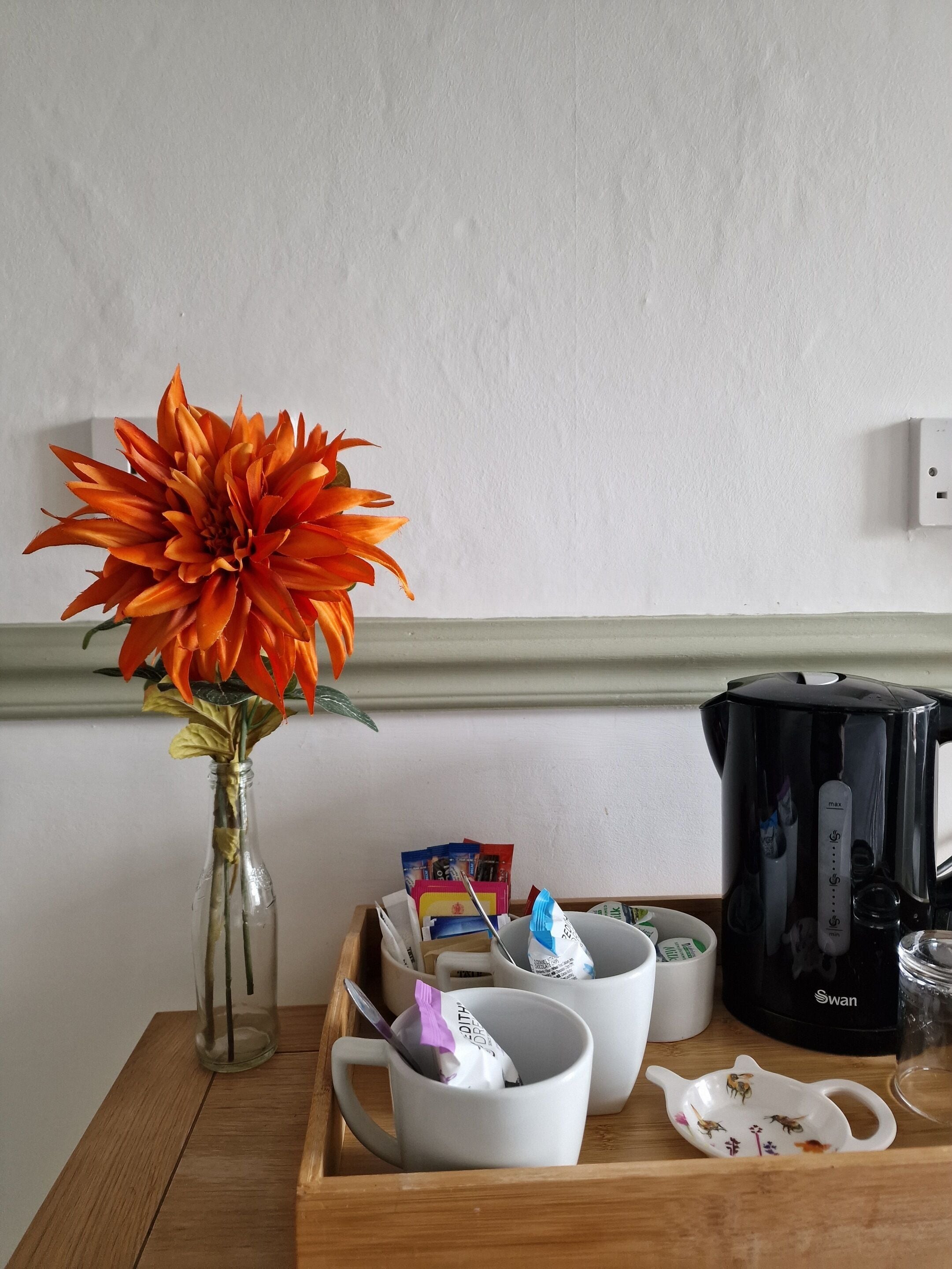 Una taula de fusta amb un ram de flors, una cafetera, tasses i un safata amb diferents objectes.
