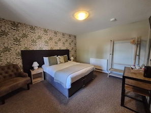 A bedroom with a bed, nightstand, lamp, chair, radiator, and a desk with items.