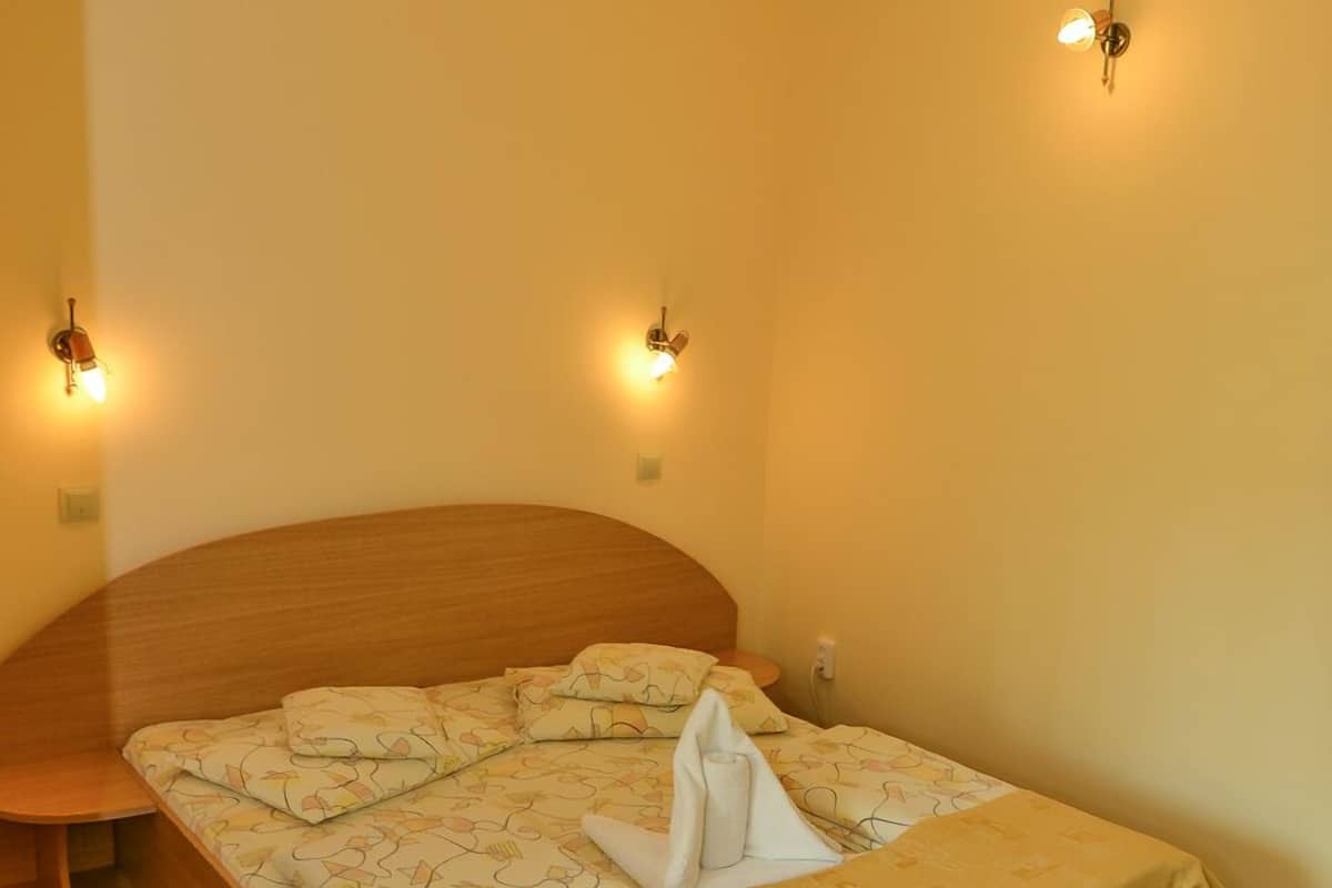 Un lit simple avec une tête de lit en bois, une couvre-lit beige et deux appliques murales.
