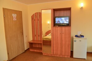 A room with a wooden wardrobe, a bed, a television, and a small refrigerator. - Pensiunea Kronstadt (Brasov)