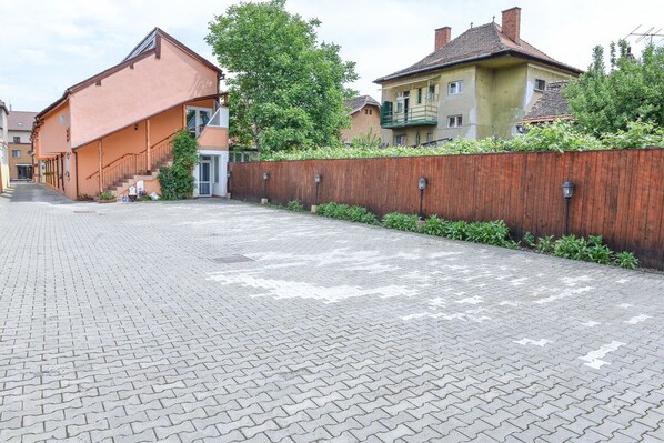 A paved walkway leading to a building with a wooden fence and greenery.