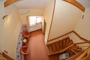 A room with a wooden staircase, a chair, a small table, and a window with curtains. - Pensiunea Kronstadt (Brasov)