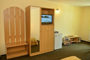 A compact room with a wooden wardrobe, a small refrigerator, a television on top of the wardrobe, and a bed with a yellow blanket. - Pensiunea Kronstadt (Brasov)