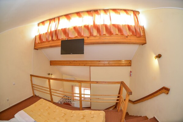 A bedroom with a bunk bed, wooden headboard, a TV mounted on the wall, and a window with curtains. - Pensiunea Kronstadt (Brasov)
