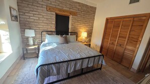 Un dormitorio con cama, mesitas de noche, lámpara, armario de madera y pared de ladrillo.