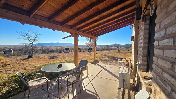 Un patio techado con una mesa y sillas, una pared de ladrillo y vistas a un paisaje seco con montañas al fondo.