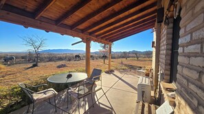 A covered patio with a table and chairs, a brick wall, and a view of a dry landscape with mountains in the distance. - Double R Guest Ranch (Elgin)