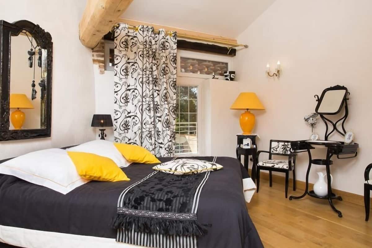 Un dormitorio con cama, dos mesitas de noche, una silla, escritorio, espejo y ventana con cortinas.