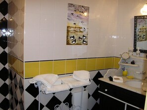 Un baño con piso a cuadros blanco y negro, una pared de acento amarilla y un cuadro de pájaros.