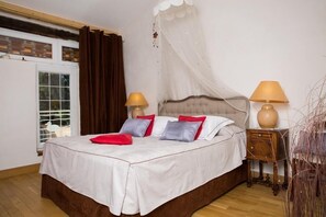 Un dormitorio con una cama, dos mesitas de noche, un ventanal y una cortina.