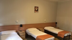 Habitación de hotel con tres camas individuales, cada una con cabecero de madera y mesita de noche con lámpara.