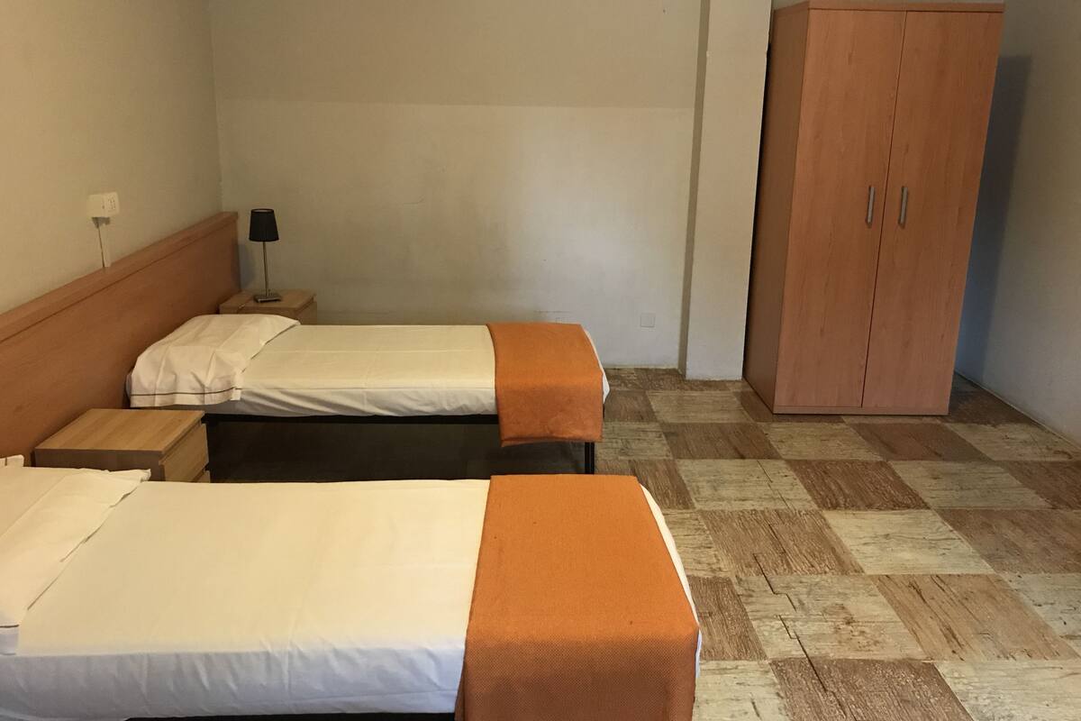 A hotel room with two beds, a wardrobe, and a nightstand with a lamp.