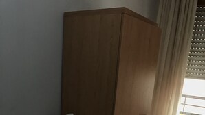 Un dormitorio con un armario de madera, una mesita de noche con lámpara y una cama con ropa de cama blanca.