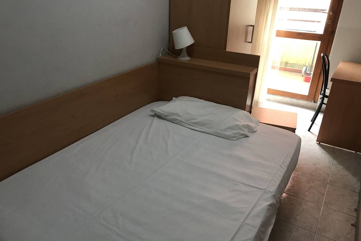 A single bed with white bedding in a room with wooden headboard and a small bedside table with a lamp.