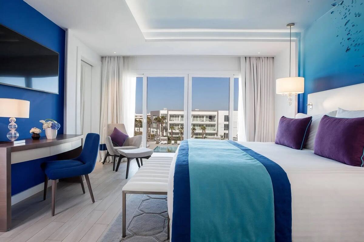 Une chambre d’hôtel avec un lit, un bureau, une chaise et de grandes fenêtres.