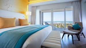 A modern hotel room with a large bed, a seating area, and a balcony with a city view. - The View Bouznika (El Mansouria)