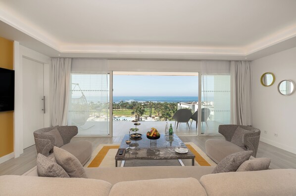 A modern living room with a large sliding glass door leading to a balcony with a view of the sea. - The View Bouznika (El Mansouria)